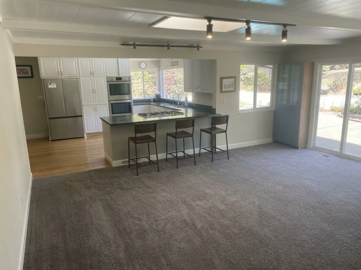 Family room carpet opening to a kitchen island with three wooden stools