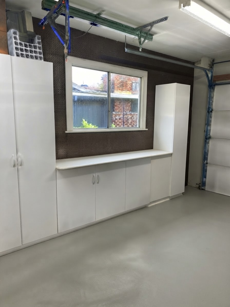 Garage wall with white cabinets, a counter under a window, and the garage door track