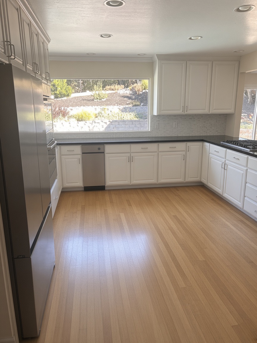 L-shaped white kitchen with light hardwood floors and a window over the counter