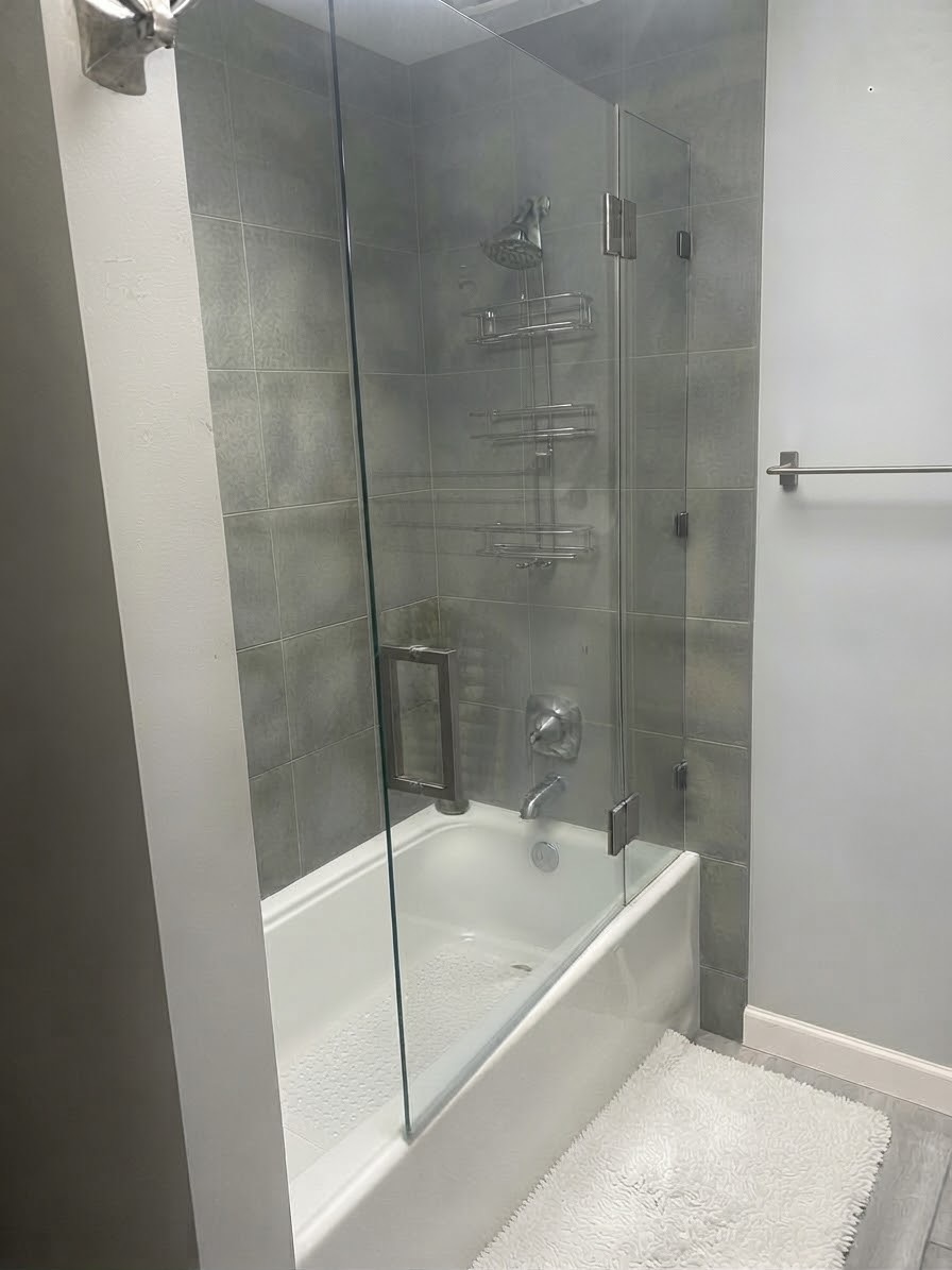 White bathtub with a glass shower screen and gray wall tile
