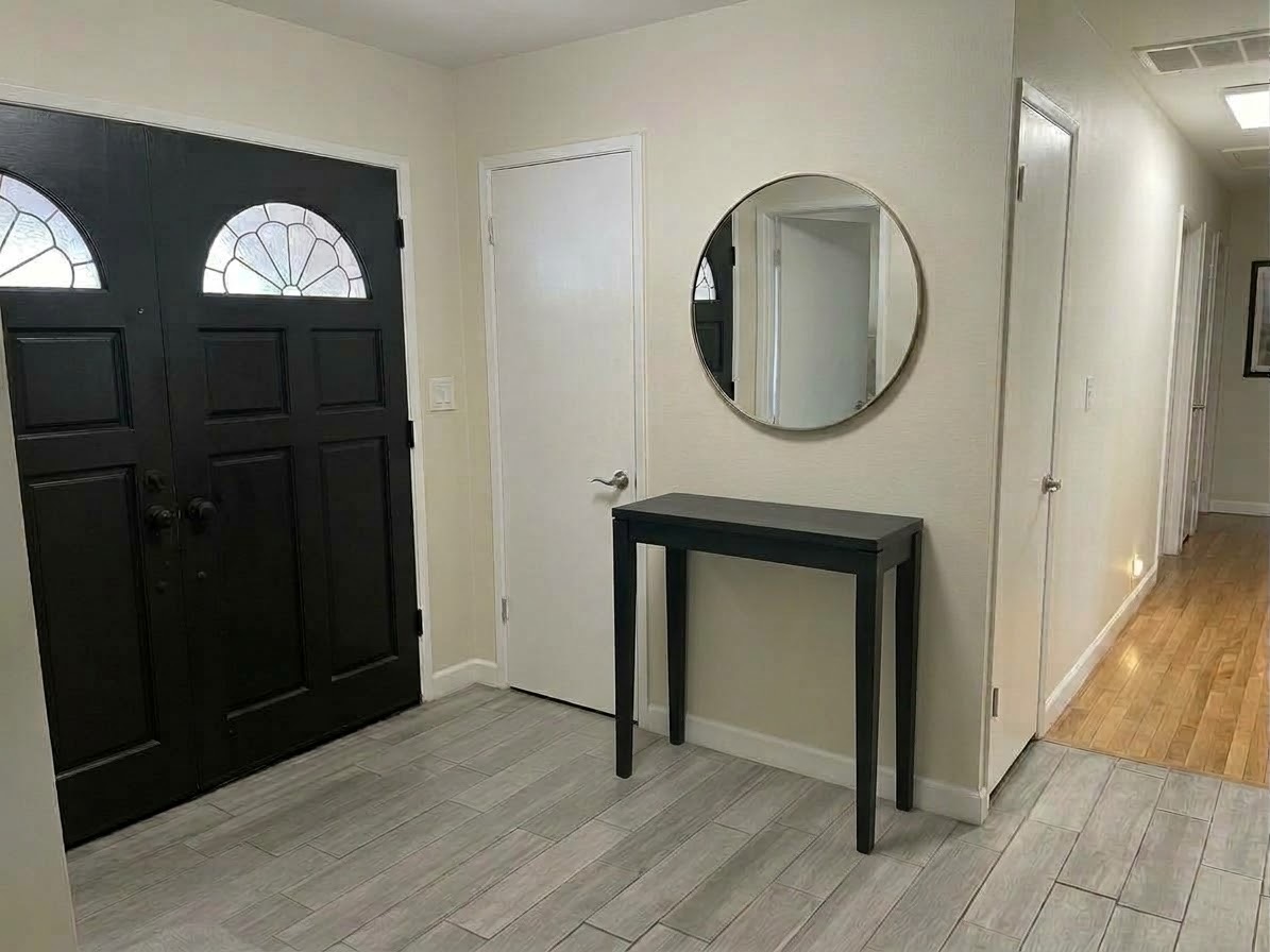 Entry with black double doors, a console table, a round mirror, and a hallway to the right