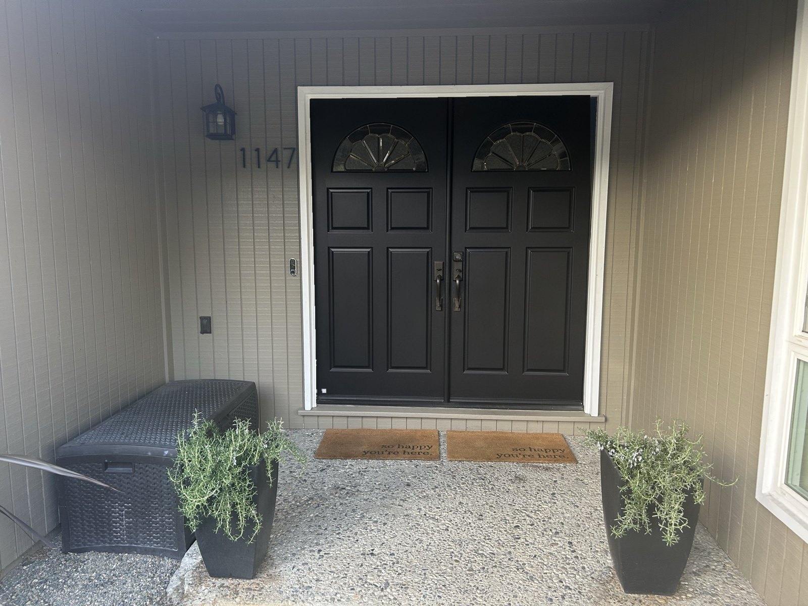 Black double front doors with fanlight windows, planters, and the number 