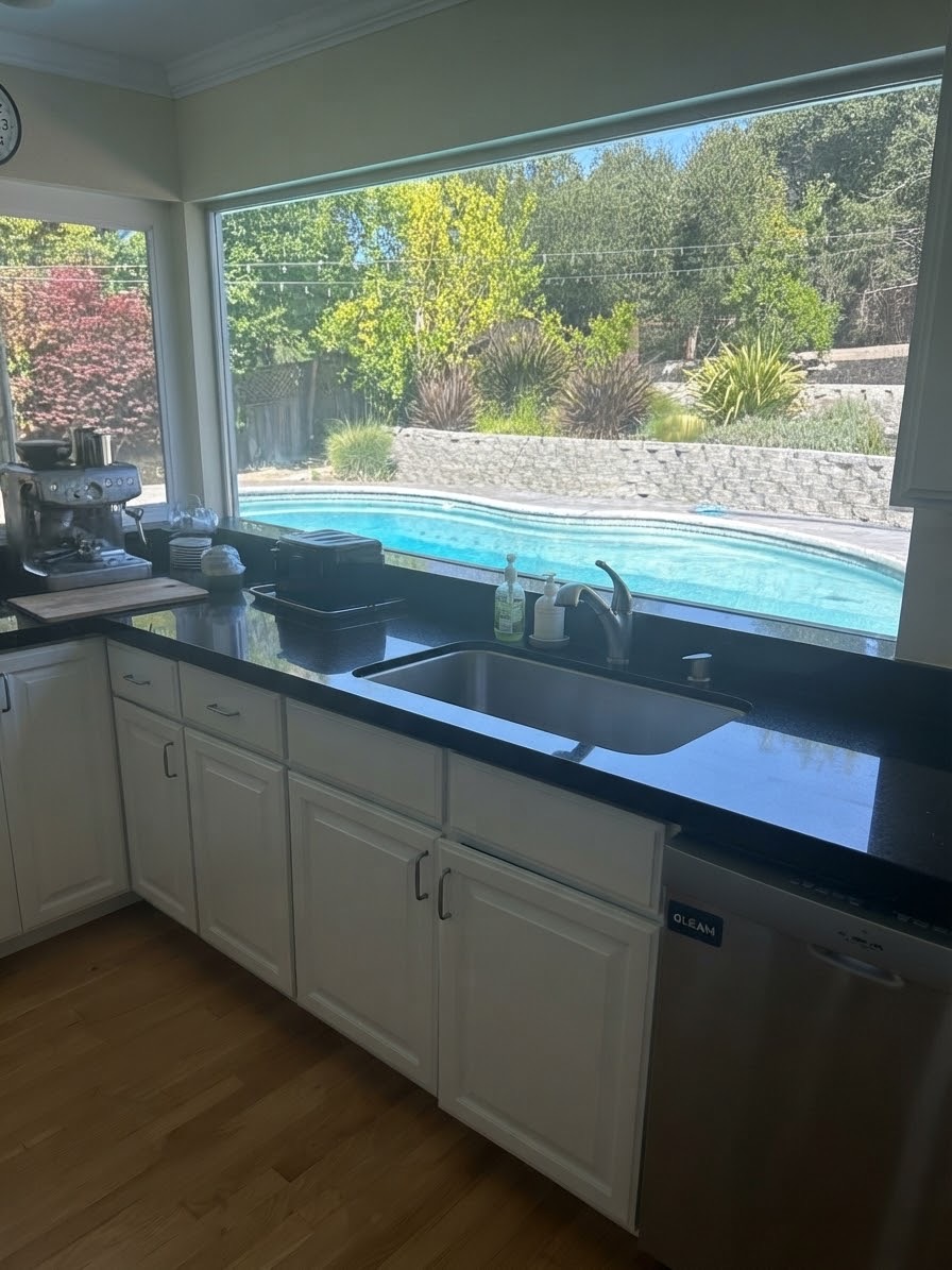 Kitchen sink under a wide window looking out at a swimming pool and garden