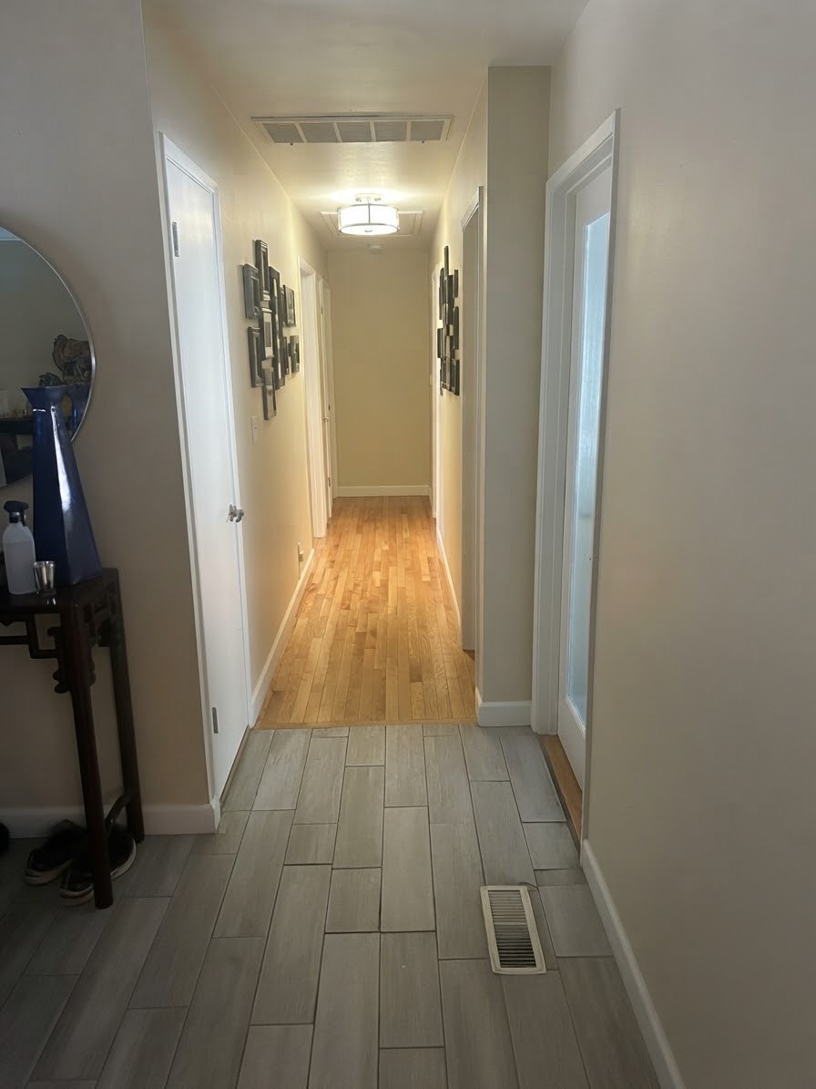 Hallway with gray tile in the foreground and hardwood floors continuing toward the bedrooms